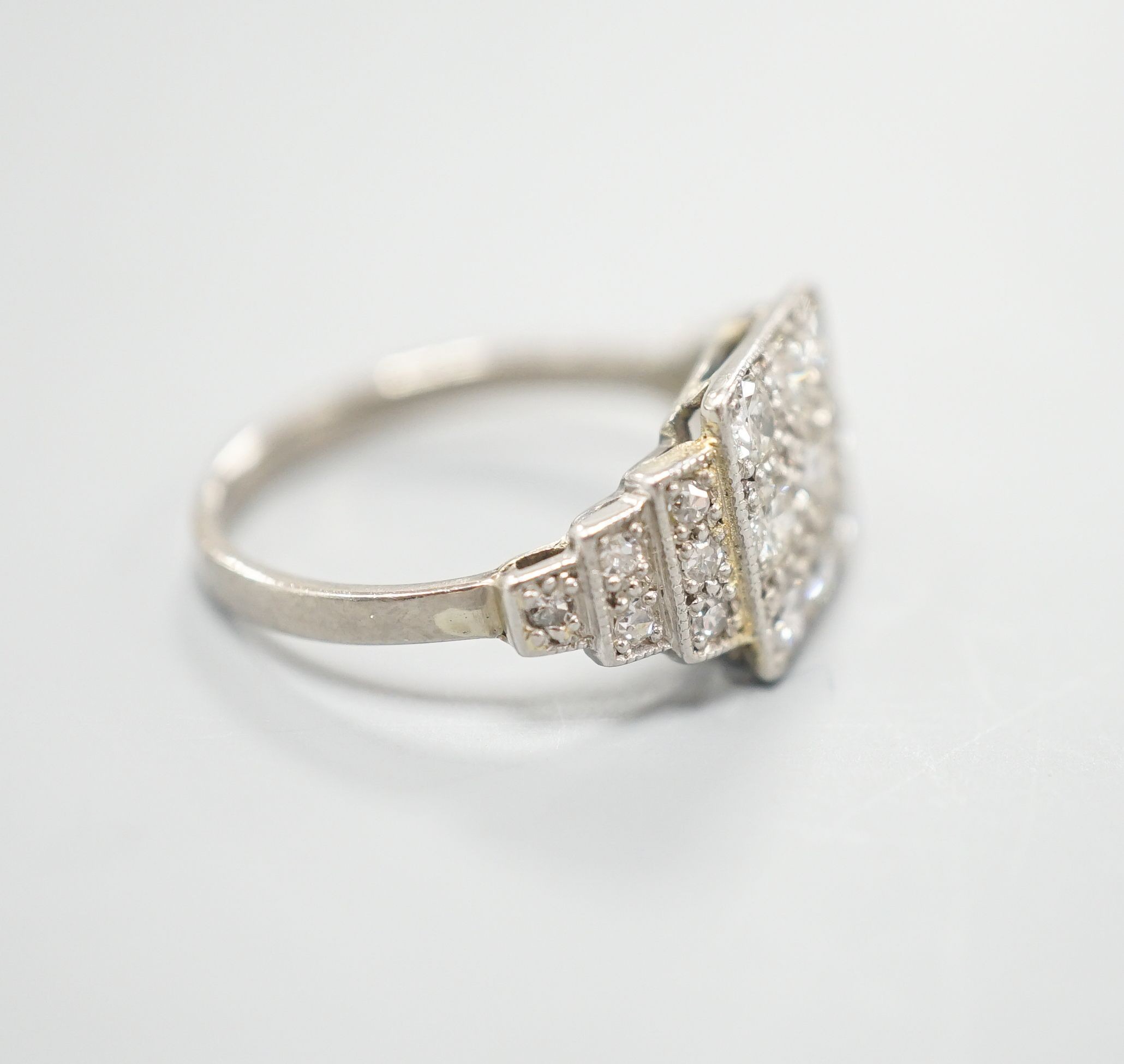 An Art Deco style white metal and nine stone diamond set tablet ring, with diamond set stepped shoulders, size K, gross weight 3.2 grams.